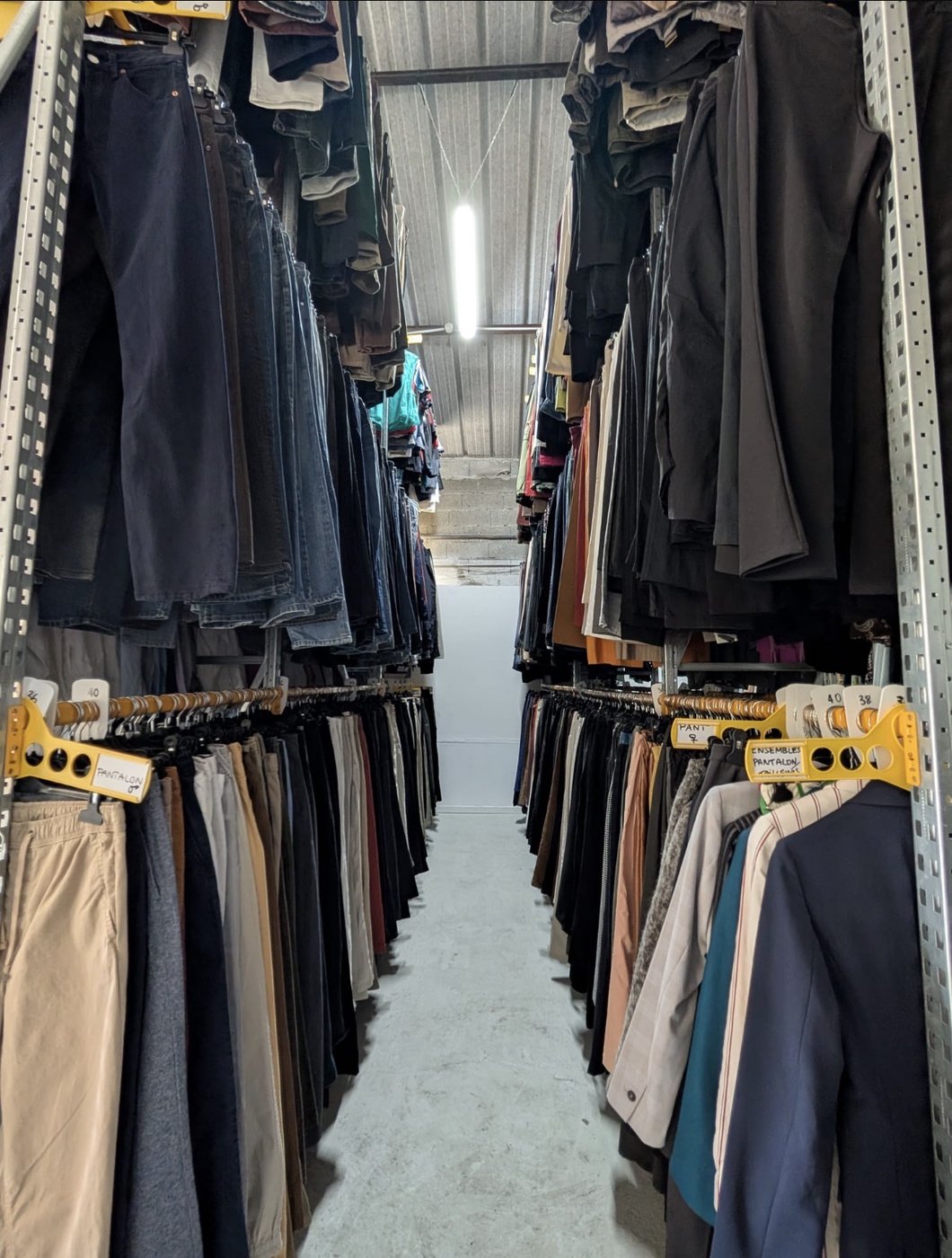 Allée de stock : pantalons et vestes hommes alignés sur portants à rouleaux