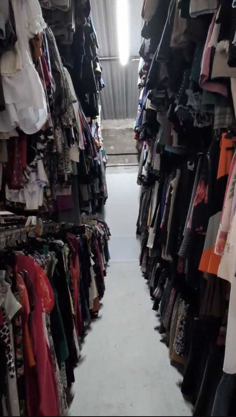 Allée de stock féminin : robes et hauts denses sur portants doubles, vue en perspective