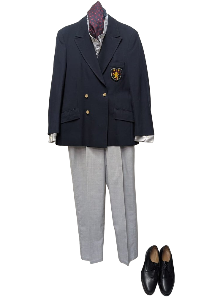 Silhouette British prep school : blazer marine double poitrine à boutons dorés et écusson héraldique au lion d'or, ascot bordeaux à motifs paisley, chemise rayée bleu/blanc, pantalon gris clair, derbies noirs