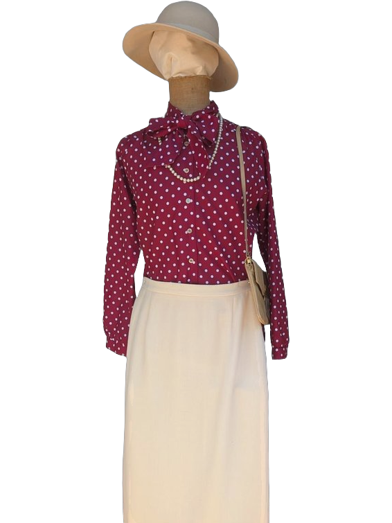 Silhouette vintage femme business années 70-80 : capeline beige, chemisier bordeaux à pois blancs avec lavallière, collier de perles, sac bandoulière beige, jupe écru longue